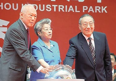 Three people stand in front of a red backdrop labeled "ZHOU INDUSTRIAL PARK" with their hands on a clear spherical object.